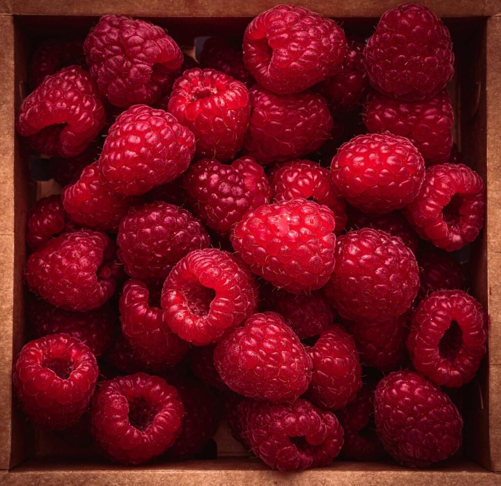 Close-up of vibrant red raspberries packed in a brown box, ideal for healthy eating.