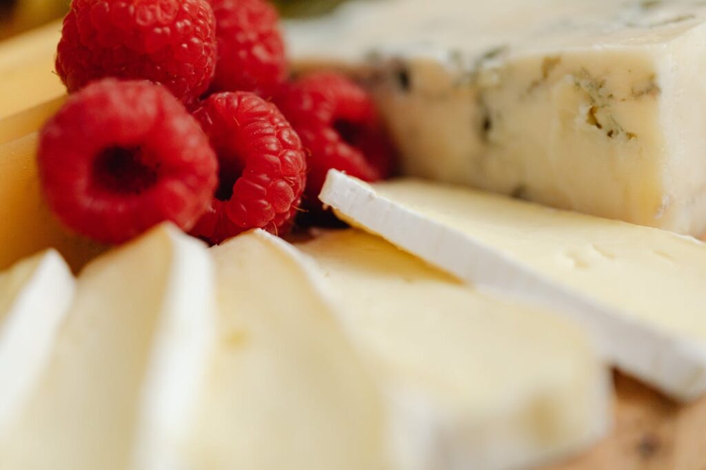 A delicious still life of various cheese types paired with fresh raspberries.